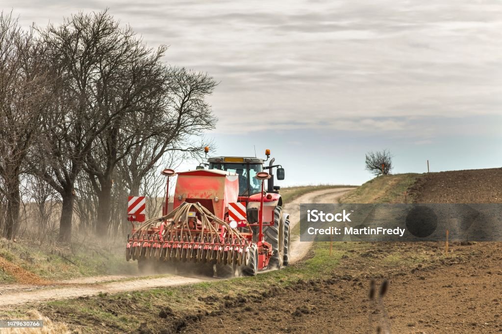 Spring work on the farm in the Czech Republic. Agricultural landscape. Spring Day on Agricultural Farm. Farmer with tractor sowing seeds of grain in his field. Growing grain. Agricultural Activity Stock Photo