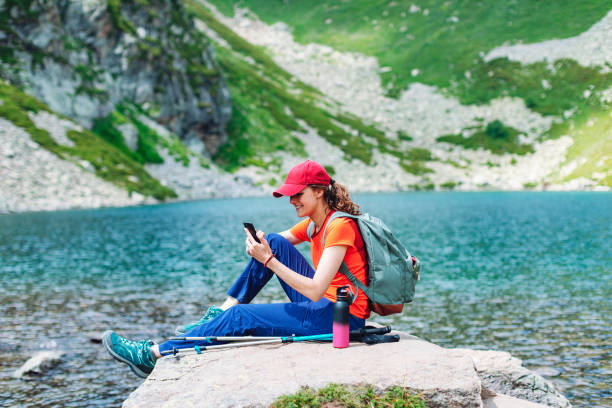istock Young woman resting near lake and using mobile while trekking in mountains 1479633984