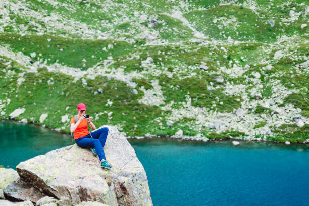 istock Young woman resting near lake and using mobile while trekking in mountains 1479637711