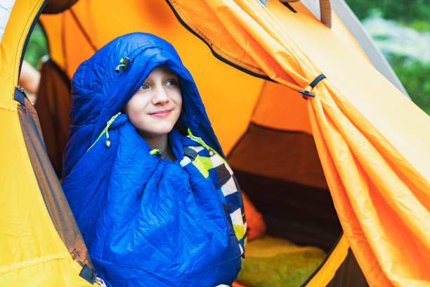 Boy in sleeping bag opening tent in the morning in mountains