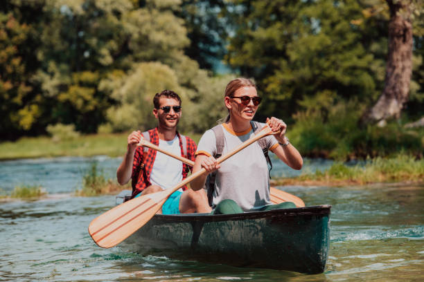 모험을 즐기는 탐험가 친구들이 아름다운 자연으로 둘러싸인 야생 강에서 카누를 타고 있습니다. - 카약 노 젓는 배 뉴스 사진 이미지