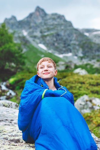 Boy in sleeping bag in the morning while trekking in mountains