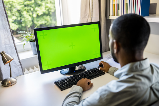 Multiracial man using computer with chroma key green screen while working at home