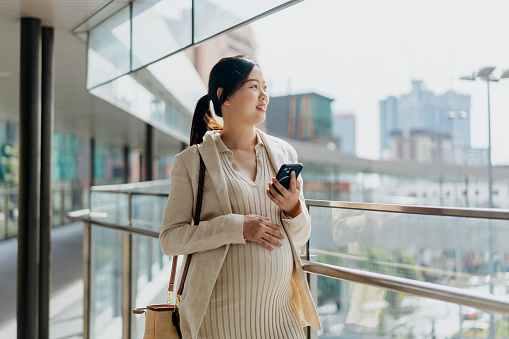 Image of a pregnant Asian Chinese businesswoman using smartphone on an elevated walkway