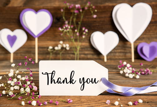 Label With English Text Thank You. Purple And Lilac Decoration And Spring Flower Arrangement. Heart Symbols With Wooden Background.