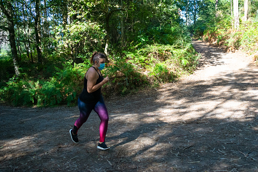 Woman with surgical mask running down a forest path in the forest