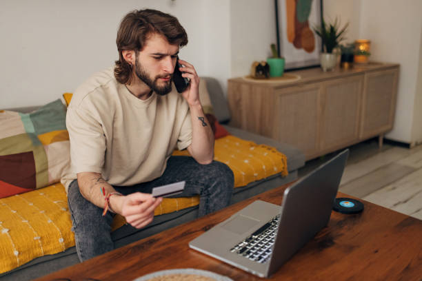 istock Confused man holding credit card in hands while using mobile phone 1479648388