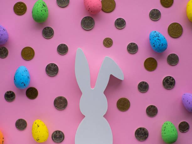 istock White Easter bunny surrounded by coins and colorful eggs on pink background. 1479648433