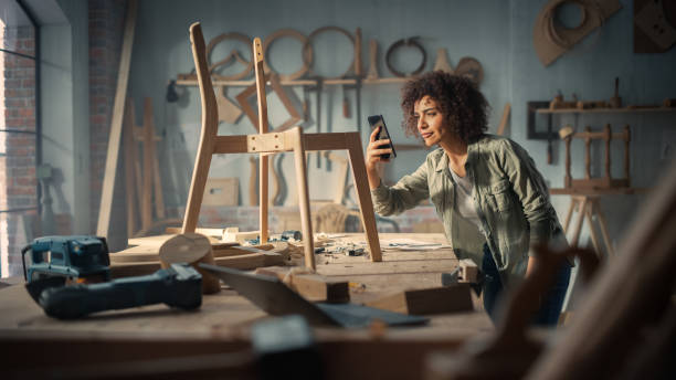 artisan product designer taking a smartphone photo of a wooden chair project. multiethnic creative female uploading picture online to her social media profile for feedback from followers and friends. - craft craftsperson photography indoors imagens e fotografias de stock