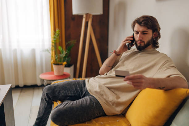 istock Handsome man sitting on sofa, making phone call while holding credit card 1479648610