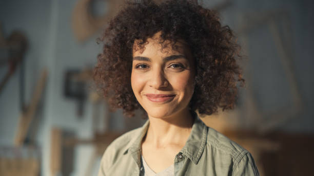close up portrait of a beautiful female creative specialist with curly hair smiling. young successful multiethnic arab woman working in art studio. dreaming about better life and opportunities ahead. - black and white portrait people women imagens e fotografias de stock