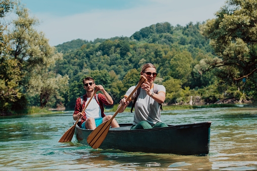 Couple adventurous explorer friends are canoeing in a wild river surrounded by the beautiful nature.