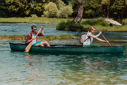 Couple adventurous explorer friends are canoeing in a wild river surrounded by the beautiful nature.