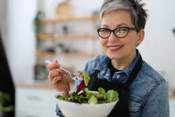 donna sorridente adulta che tiene un piatto con insalata fresca, pranzo dietetico. - salad food and drink food lettuce foto e immagini stock