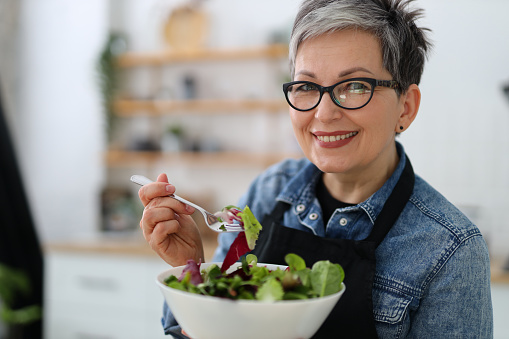 Adult smiling woman holding a plate with fresh salad, diet lunch.