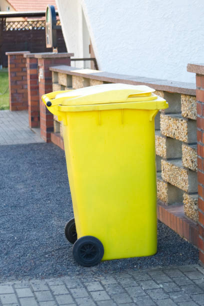 Yellow garbage container near the stone fence close-up