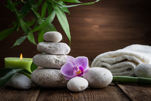 White Zen balance stones, an Orchid flower, a bamboo plant and a candle on a wooden table