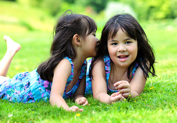 Two little girls telling a secret, lying on a grass in the park