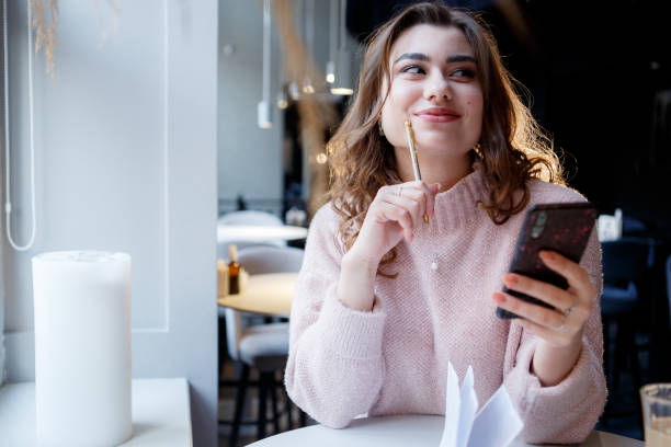 istock Cheerful female student with smile sitting at table in cafe reading information on mobile phone. 1479669544