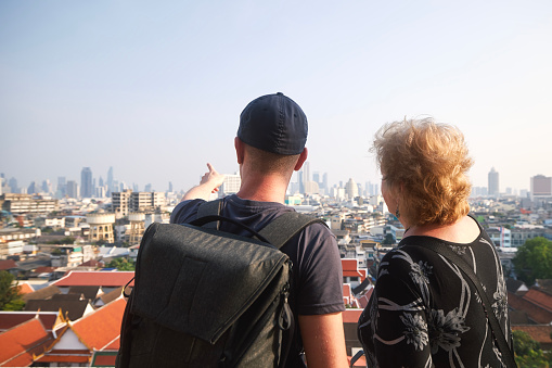 Two tourists in Bangkok. Adult man is traveling with his senior mother and showing her urban skyline view with landmarks and skyscrapers.