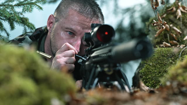 SLO MO LD Male sniper looking through the scope of his rifle and ejecting an empty bullet casing
