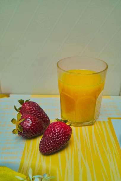 GLASS OF ORANGE JUICE WITH THREE STRAWBERRIES ON TABLECLOTH
