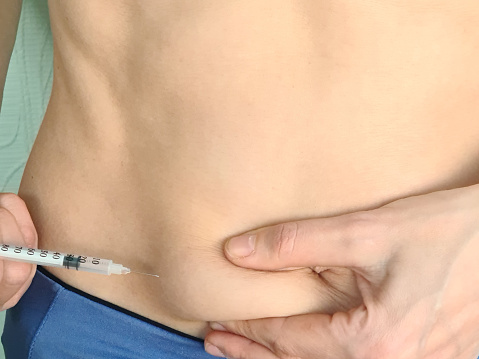 Woman inserts needle and syringe into abdomen. Pregnancy and hormone therapy