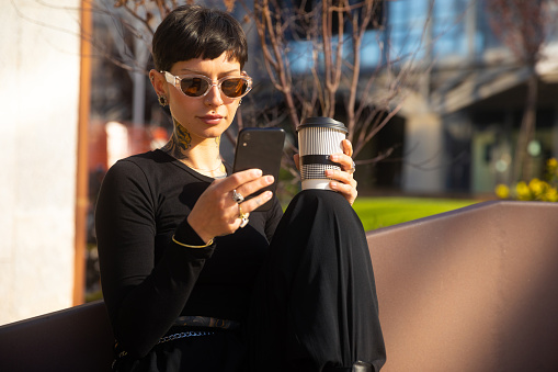 Beautiful woman with short hair portrait outdoor in the city using smartphone and drink coffee