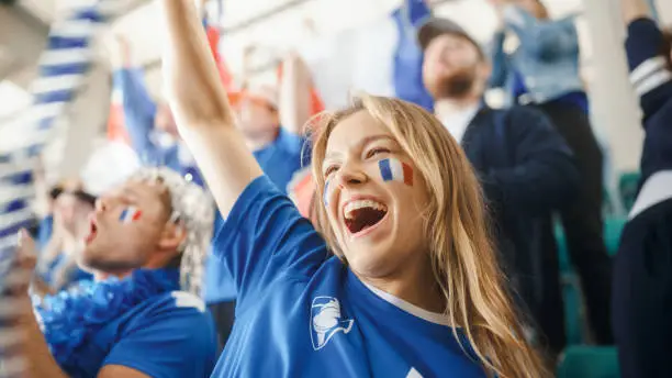 Photo of Sport Stadium Big Event: Portrait of Beautiful Sports Fan Girl with French Flag Painted Face Cheering For Her Team to Win. Crowd of Fans Shout, Celebrate Scoring a Goal, Championship Victory