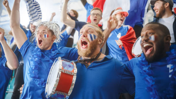 istock Sport Stadium Big Event: Three Fans with Painted Faces Cheering, Beating the Drum, Having Fun, Shout for Soccer Team to Win. People Celebrate Scoring a Goal, Championship Victory 1479681537