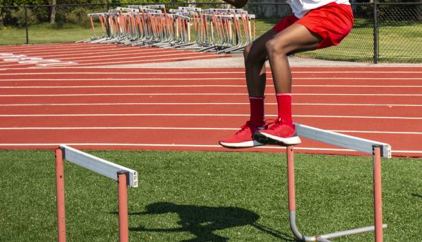 African American athlete juming over track hurdles