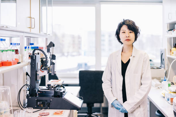 Female Japanese scientist stands alone in a laboratory With a singular focus on scientific innovation and discovery, a lone Japanese researcher poses for a portrait in a high-tech laboratory, projecting a sense of quiet competence and expertise as they gaze intently at the camera. 3d printing lab stock pictures, royalty-free photos & images