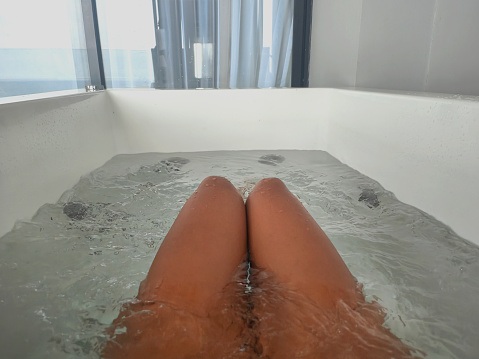 Close-up POV unrecognizable woman sitting inside a hot tub with jets on. Her knees piercing the top surface of the water