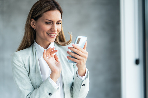 Young beautiful business woman texting in the office. Smiling woman with smart casual businesswear using smartphone for business communication on surfing the net while take a break