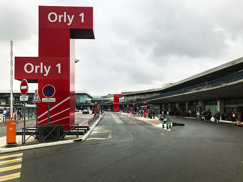 Orly airport entrance in Paris. People arriving for their flight, carrying their luggage, entering through the main gate.