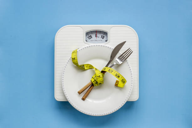 istock Weight scale and tape measure over dinner fork and knife on the plate 1479693722