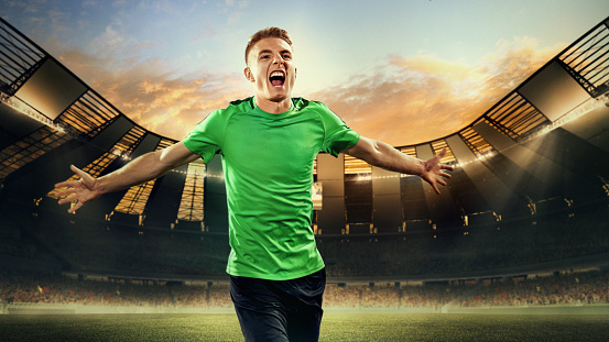 Winning emotions. Happy young man, football player running with happy emotions on 3D open air football stadium with blurred background. Concept of match, sport, competition, action and motion, game