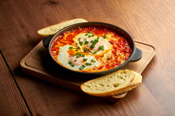 Fried eggs with tomatoes, onions and pita bread in a pan on a wooden background. Tasty Shakshuka stock photo