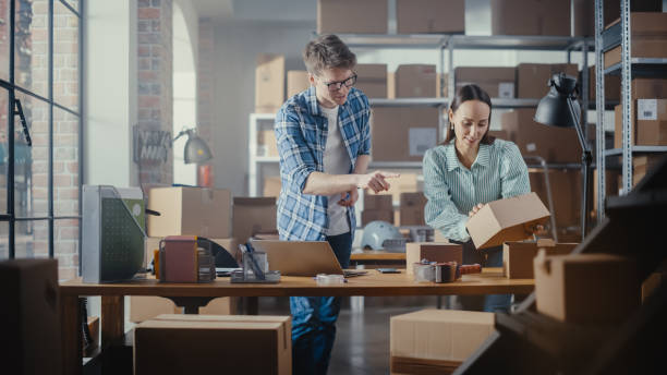 istock Happy Young Male and Female Working in Warehouse. Talking, Using Laptop Computer, Checking Retail Stock, Preparing Shipment. Successful Small Business Owners High Five Each Other. 1479701918