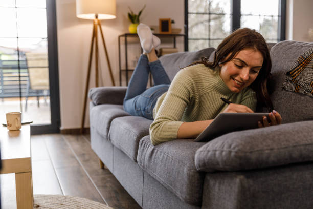 istock Young woman lying on the sofa and drawing on tablet with digitized pen 1479707299