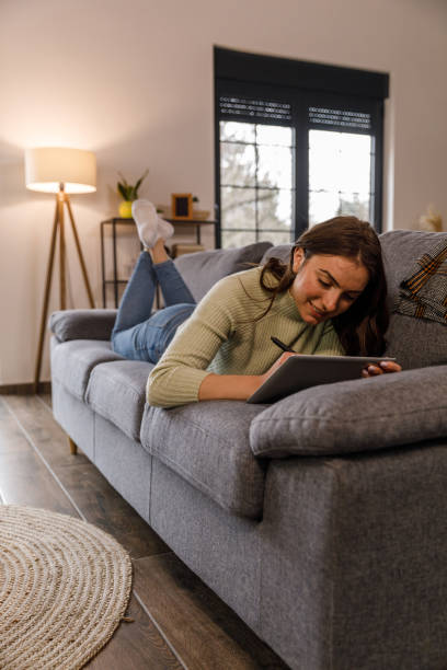 istock Young woman lying on the sofa and drawing on tablet with digitized pen 1479707438