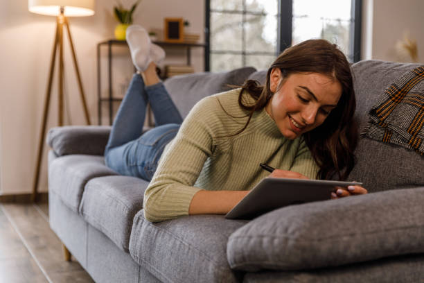 istock Young woman lying on the sofa and drawing on tablet with digitized pen 1479707491