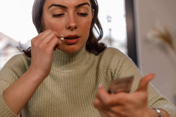 giovane donna che legge un'etichetta su un pacchetto di pillole mentre prende il suo farmaco - blister packaging foto e immagini stock