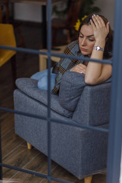 istock Sad young woman sitting on the sofa, wrapped in a blanket, contemplating problems and solutions 1479708448