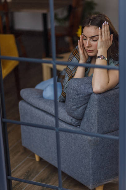 istock Sad young woman sitting on the sofa, wrapped in a blanket, contemplating problems and solutions 1479708454