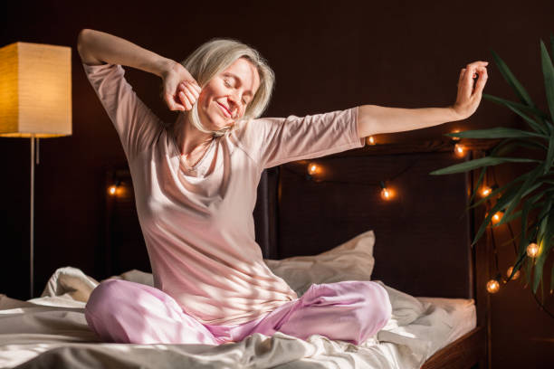 istock Happy middle aged woman sits on bed and stretching arms 1479710347