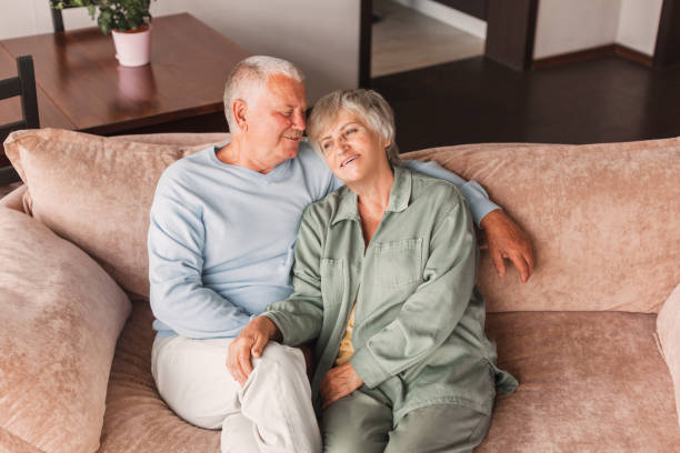 自宅のソファに座って抱き合う美しい老夫婦のポートレート - senior adult retirement mature adult couple ストックフォトと画像