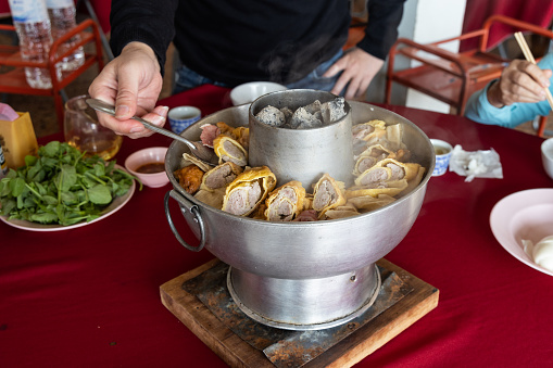 Diner preparing Yunnan hotpot in Ban Rak Thai restaurant within Mae Hong Son province, Thailand. Fueled with charcoal, hotpot ingredients include fish and meat cake wrapped in tofu skin and vegetable