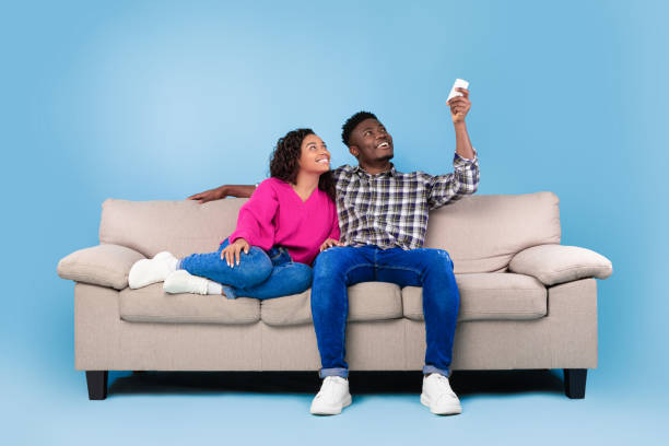 istock Split system. Young black couple with remote relaxing under air conditioner, sitting on couch over blue background 1479721828