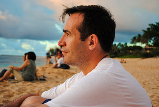 Side view of a young handsome man watching the sunset in Sunset Beach, Oahu, Hawaii, USA
